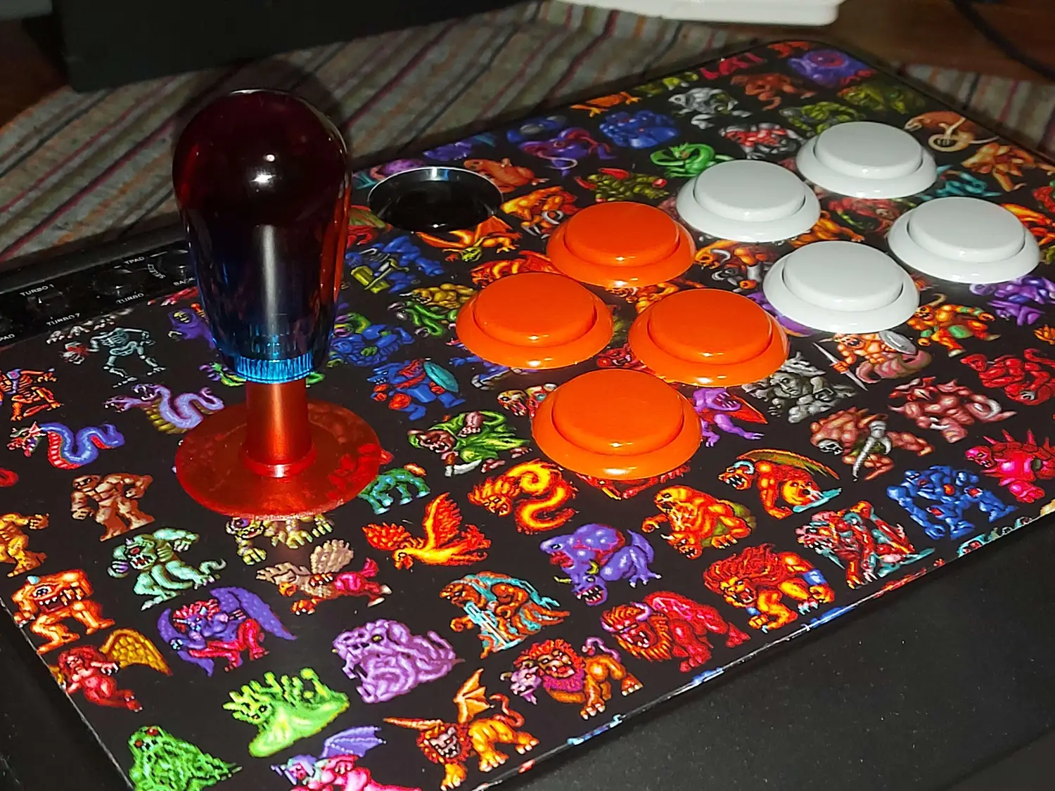 The arcade stick I use to play shmups: a Mayflash F300 with Sanwa buttons and a Seimitsu LS-56-01 lever with a bat top. The graphic is a grid of monster sprites from Last Armageddon. The buttons are 4 orange on the left and 4 grey on the right.